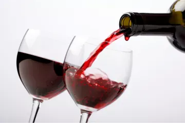 A bottle filling two wine glasses with red wine.