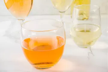 A selection of wine glasses on a table, featuring an orange wine in a stemless glass in the foreground and several glasses of white wine and one more of orange wine in the background.
