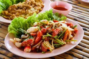 A plate of Thai spicy seafood salad with squid, crab sticks, fresh herbs, and vegetables, served with lettuce and dipping sauce