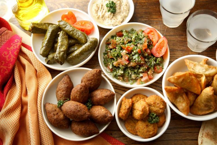 Top view of a mezze platter with stuffed grape leaves, kibbeh, tabbouleh, and assorted dips with pita bread on a wooden table