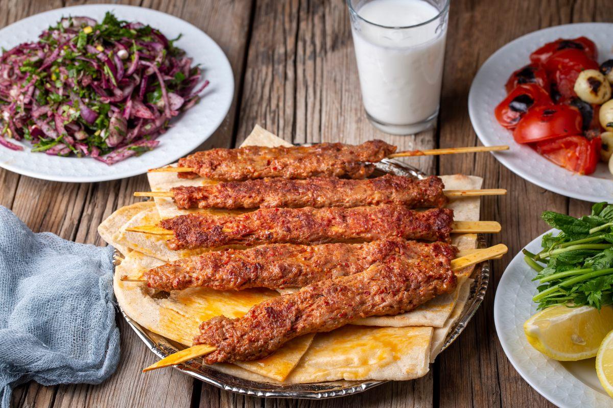 A few Adana kebabs on flat bread with accompanying dishes.