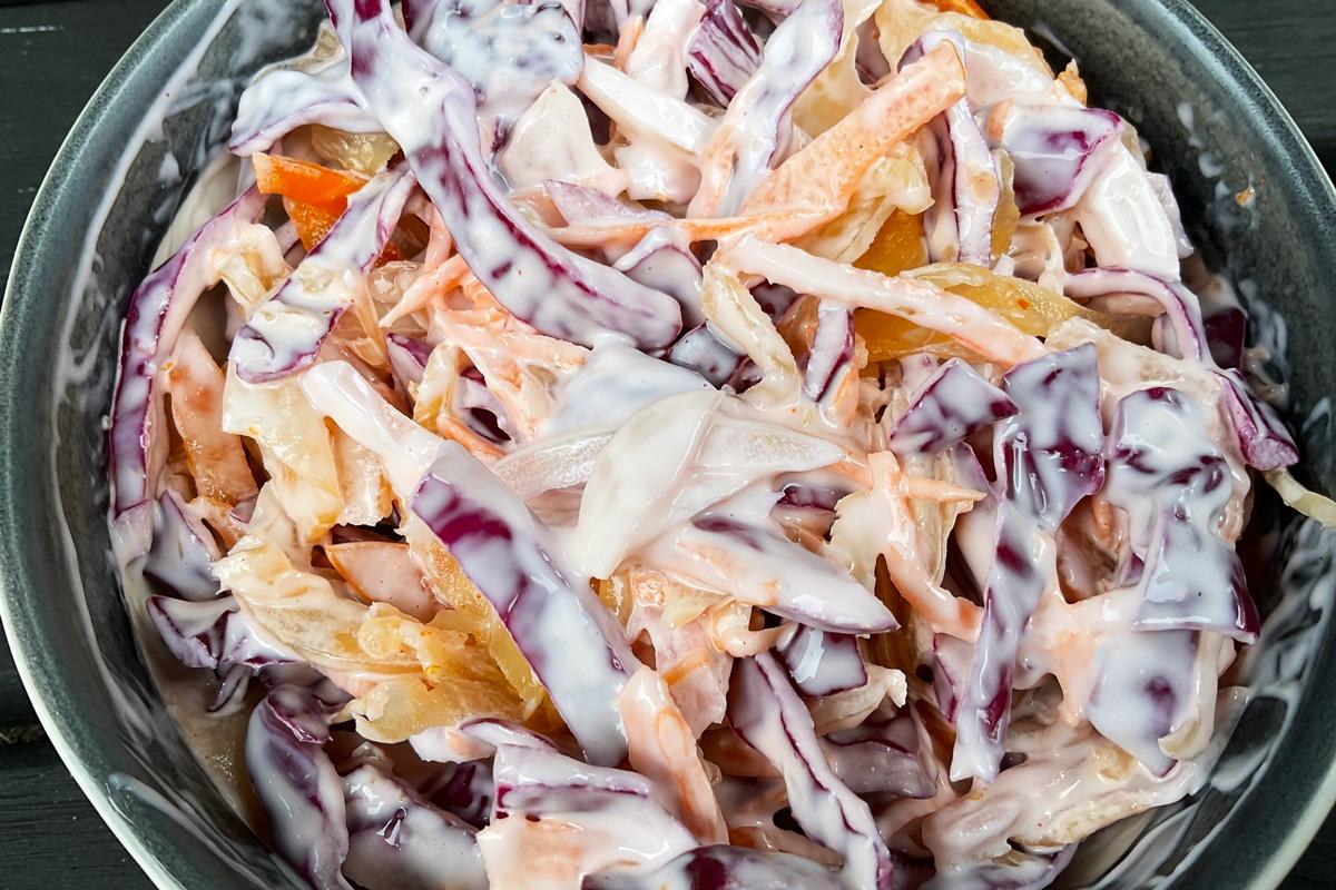 A bowl of kimchi coleslaw featuring shredded red cabbage, kimchi mixed with carrot and onion, coated in a creamy dressing