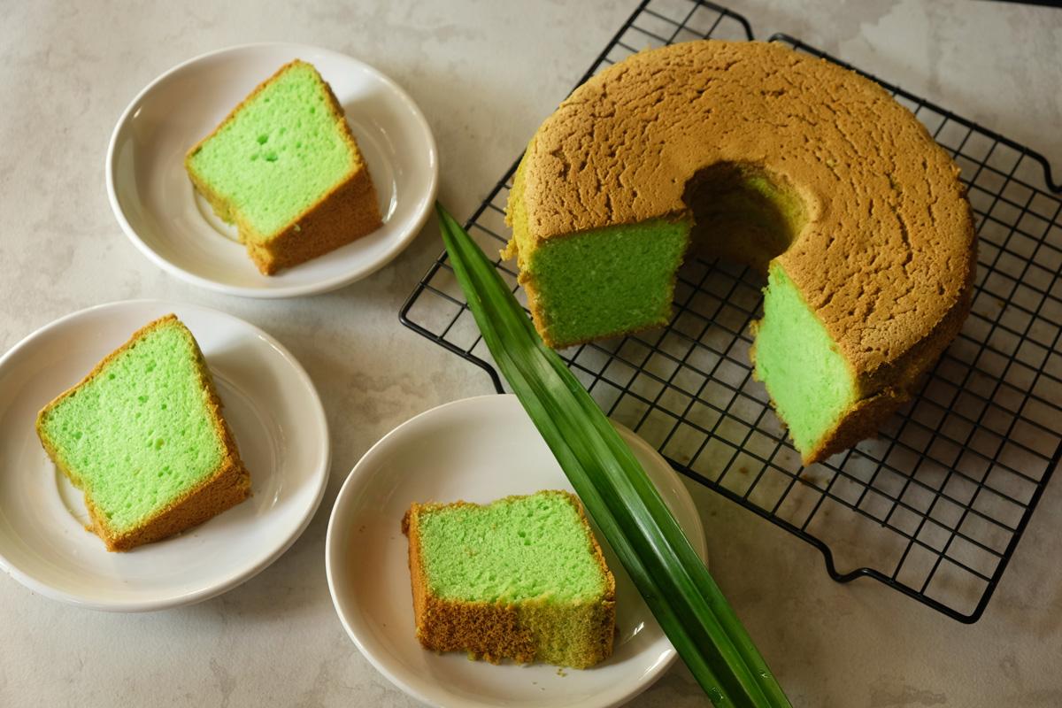 A pandan chiffon cake, with a piece cut out, resting on a grid support with three slices on serving plates in front.