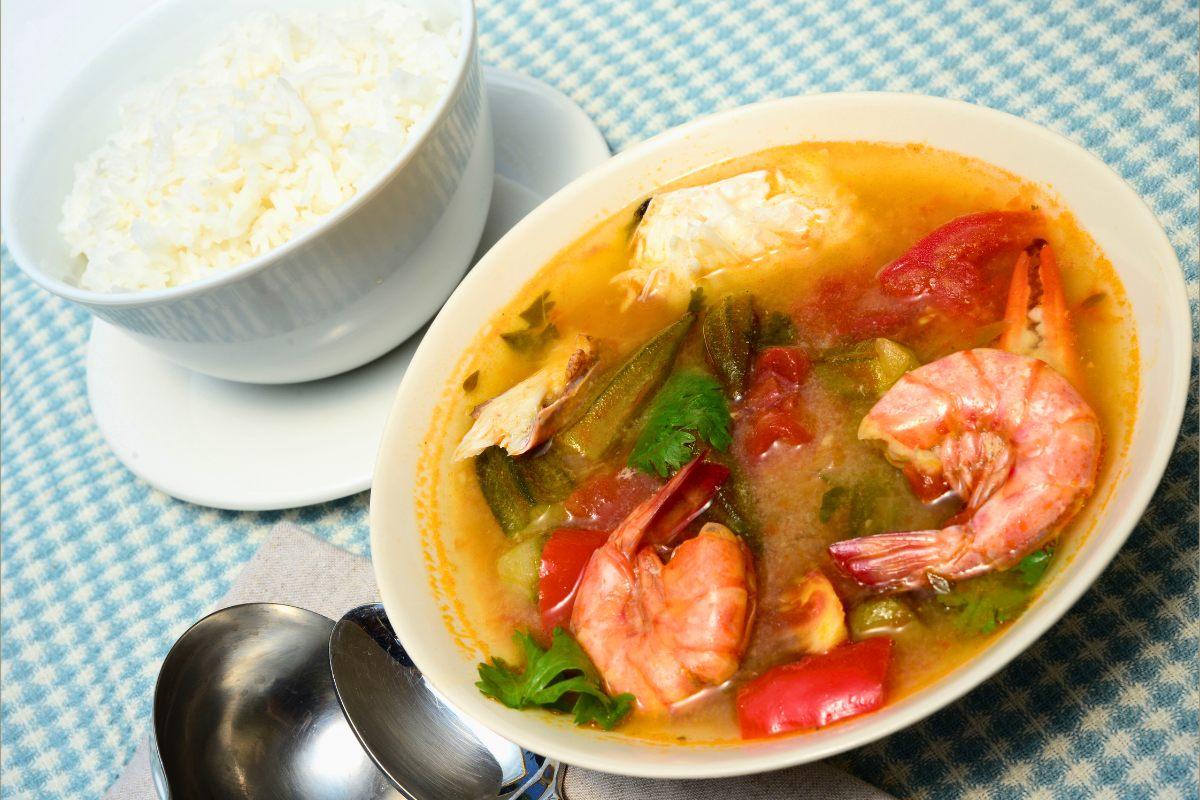 A bowl of crab, shrimp and okra gumbo with a small bowl of rice on a plate on the side.
