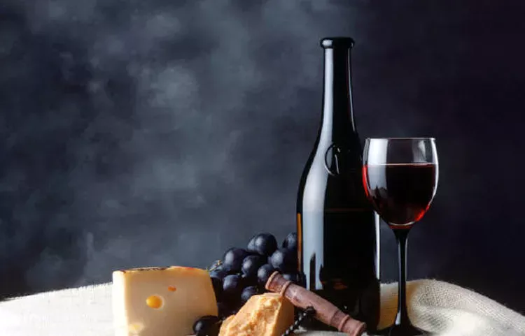 A bottle anda glass of red wine with grapes, cheese and bread.