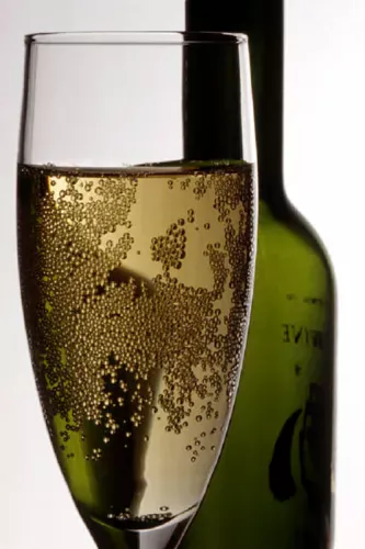 A glass of sparkling wine with a bottle in the background.