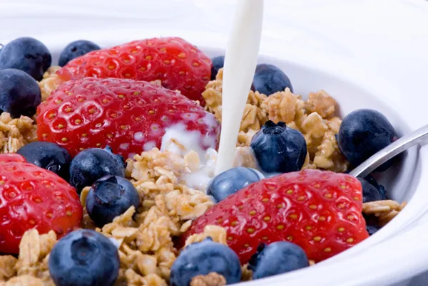 Pouring milk on breakfast granola, strawberries and blueberries.