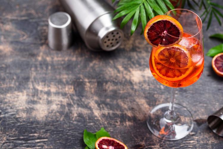 Blood orange spritz with slices of blood orange on a rustic surface with a shaker and jigger in the background.