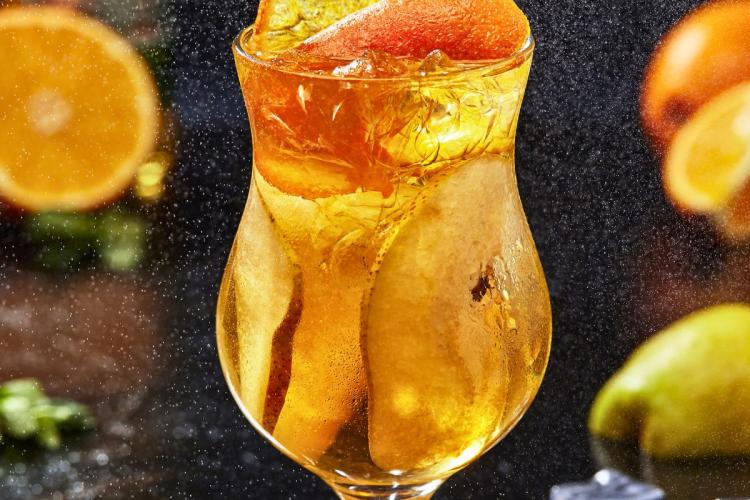 Cider spritz cocktail with ice and slices of orange in a curved glass against a misty, festive background.