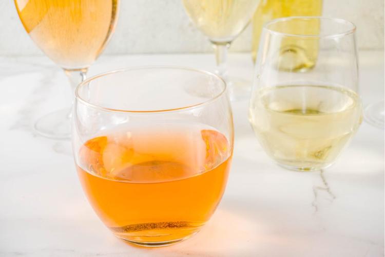 A selection of wine glasses on a table, featuring an orange wine in a stemless glass in the foreground and several glasses of white wine and one more of orange wine in the background.