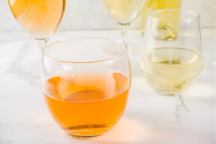 A selection of wine glasses on a table, featuring an orange wine in a stemless glass in the foreground and several glasses of white wine and one more of orange wine in the background.