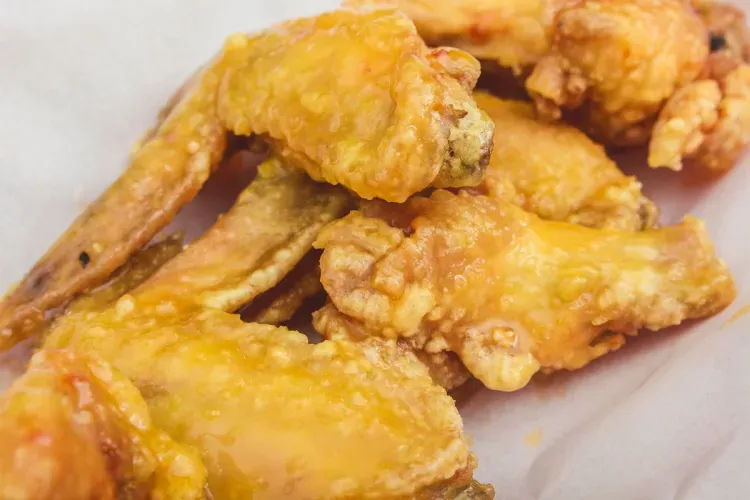 Close-up of crispy chicken wings coated with a glossy citrus glaze, showcasing a golden-brown crust and a sticky yellow-orange finish.