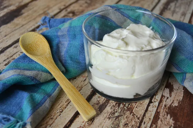A glass filled with thick Icelandic skyr, accompanied by a wooden spoon and a blue checkered napkin on a rustic table.