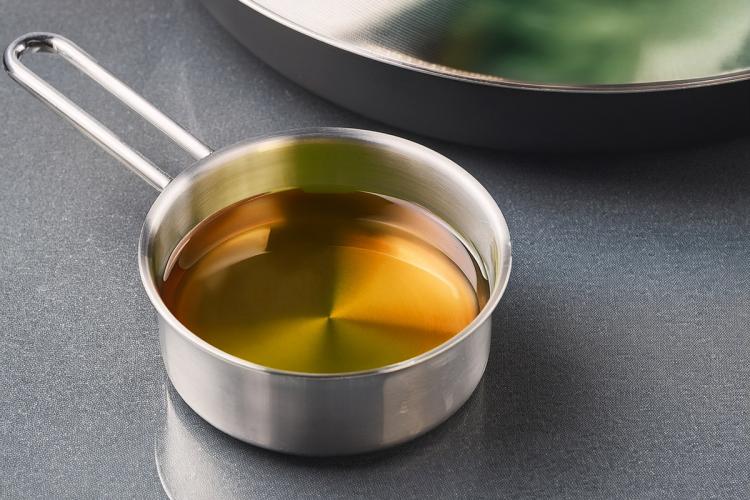 Small stainless saucepan filled with algae oil on a gray kitchen surface.