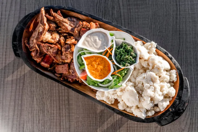 Swazi or Eswatini platter with braaied meat left, white pap right, with greens, salad, and sauces in the center.