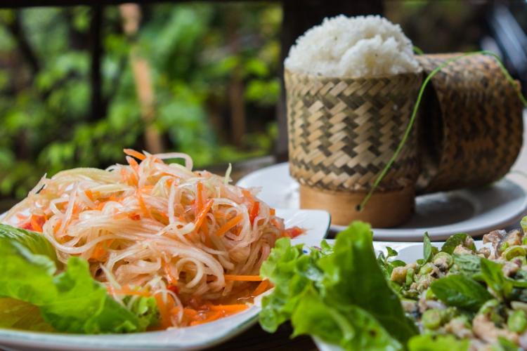 A plate with spicy papaya salad, fish barb and sticky rice in a bamboo basket.