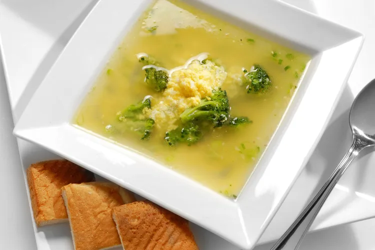Bowl of sopa de huevo with broccoli in light broth, served with bread.