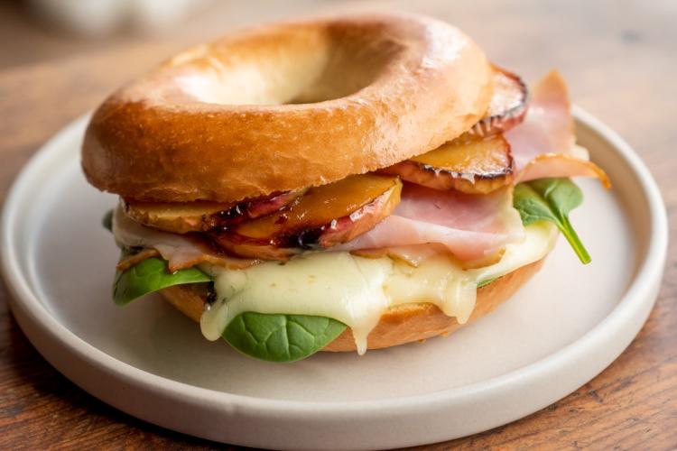 Bagel sandwich with ham, melted cheese, spinach, and grilled apple slices on a ceramic plate.
