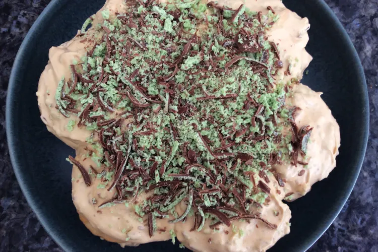 Overhead view of a whole peppermint and chocolate tart on a dark plate, generously topped with green mint chocolate and dark chocolate shavings.
