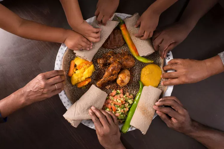 Several people sharing an Ethiopian meal and using pieces of injera to pick up the food.