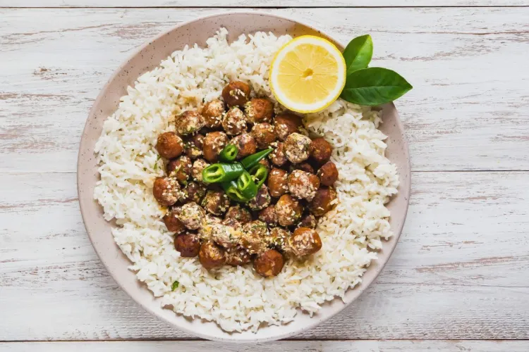 A plate of Egyptian shrimp kofta — small golden-fried shrimp croquettes sprinkled with sesame seeds and herbs — arranged over a ring of white rice and topped with sliced green chile and half a lemon.