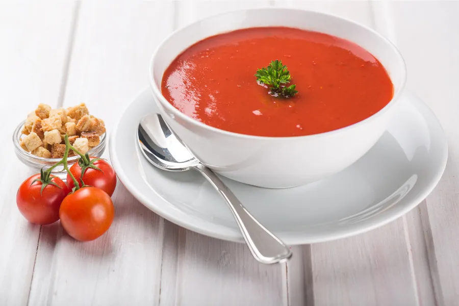 A bowl of tomato soup decorated with basil leaves.