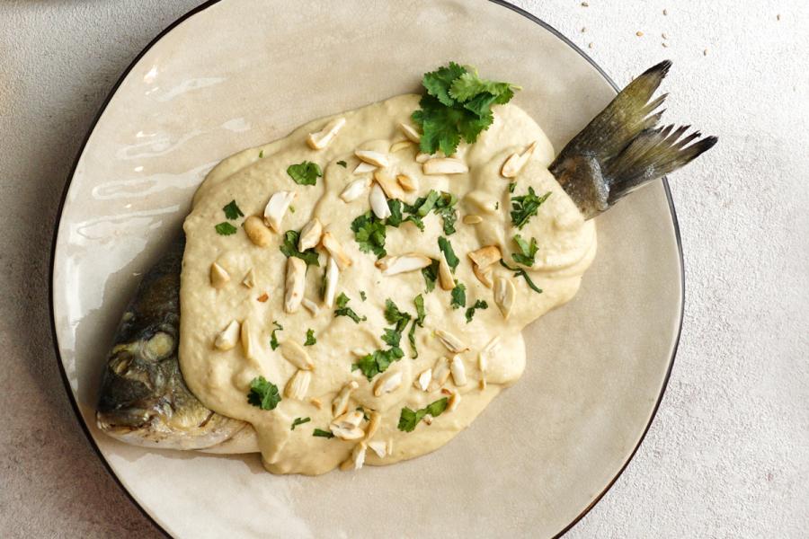 Whole fish covered in tahini sauce, garnished with chopped almonds and fresh parsley.