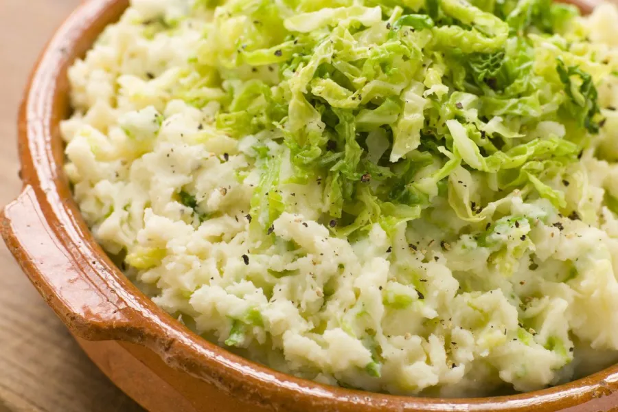 A traditional Irish dish made of mashed potatoes mixed with finely chopped cabbage. The dish is served in a rustic ceramic bowl and sprinkled with black pepper.
