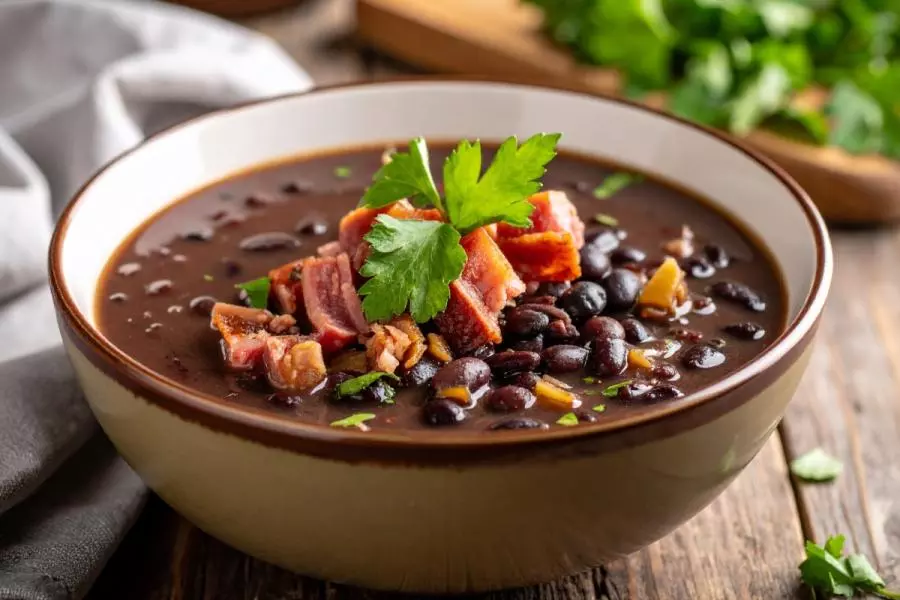 Close-up of black bean soup with whole beans, topped with diced ham hock and fresh parsley - synthetic image.