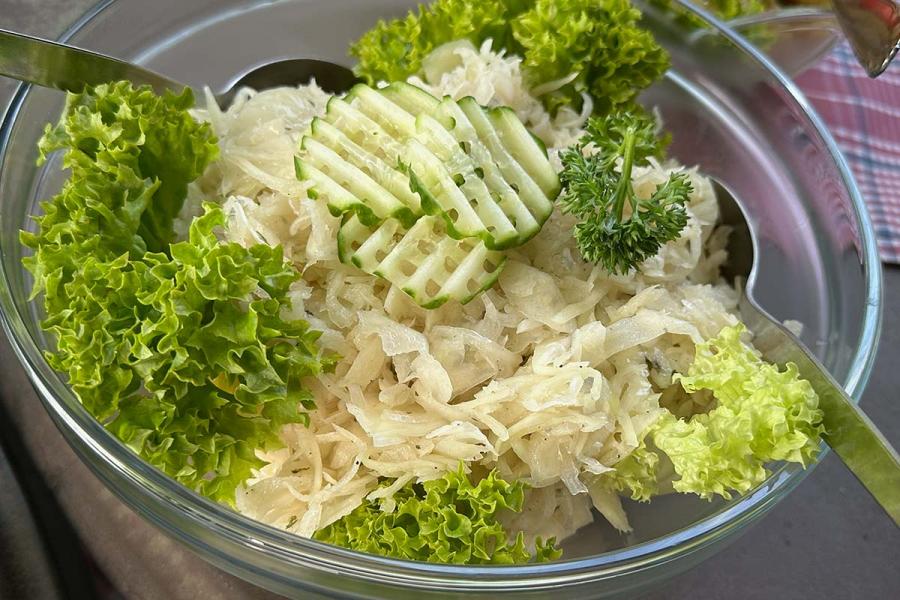 German raw cabbage salad made with shredded white cabbage, garnished with cucumber slices and parsley, served on a bed of green lettuce in a glass bowl.