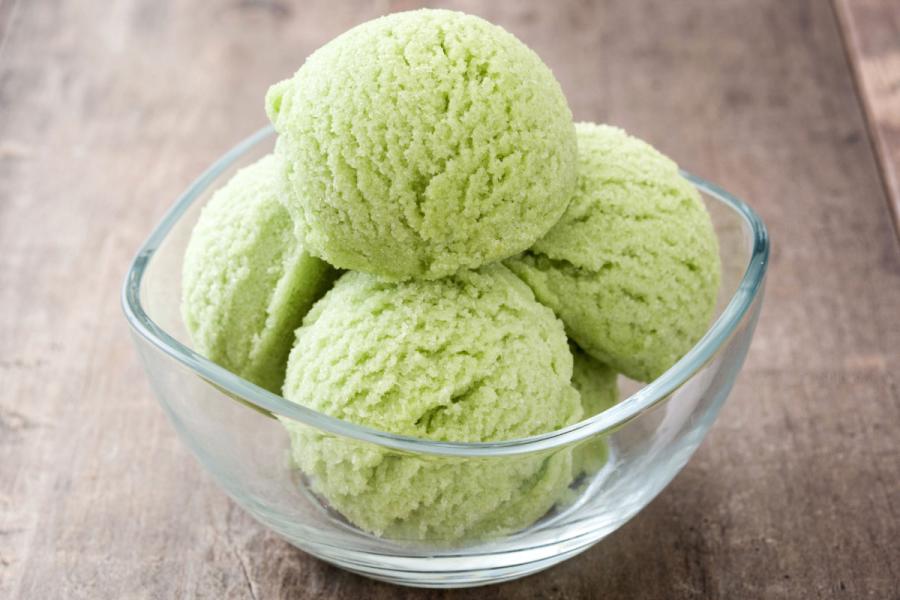 Four scoops of matcha ice cream in a glass bowl with a square rim.