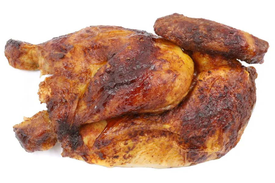 Whole spit-roasted chicken with deeply browned, crisp skin, spatchcocked and photographed from above on a plain white background