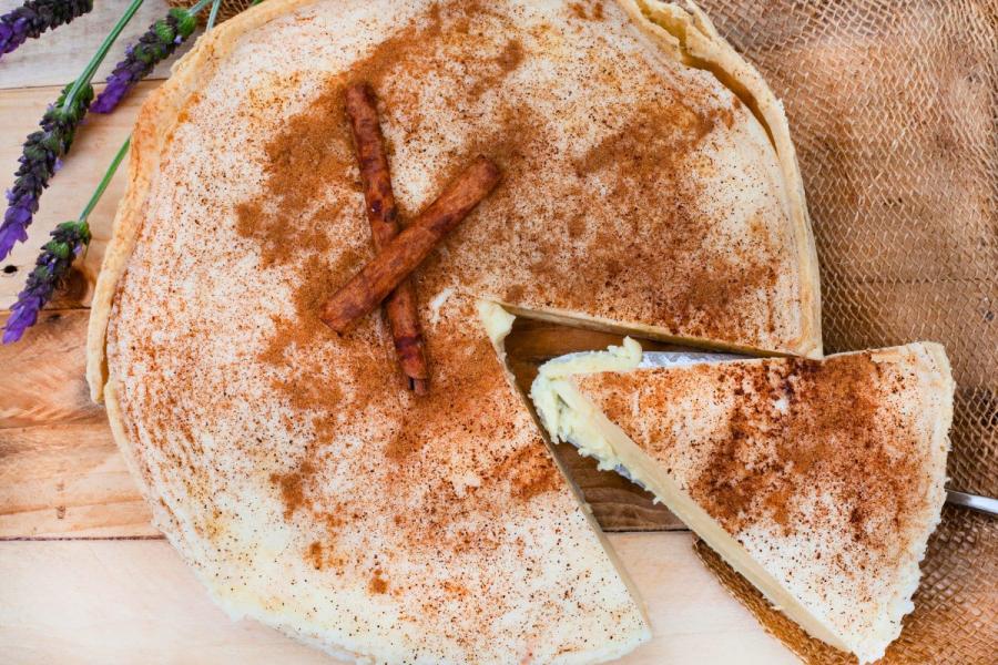 A whole melktert, sprinkled with cinnamon, with a piece cut out. 