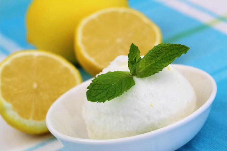 Bowl of lemon mint sorbet with fresh mint leaves, surrounded by halved and whole lemons.